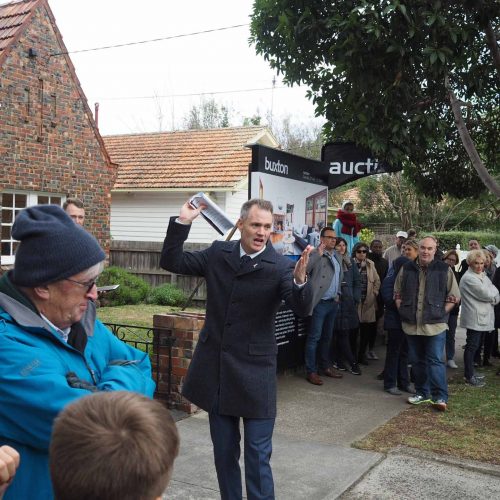 Auction snapshot - Auctioneer calling auction in front of brown brick house