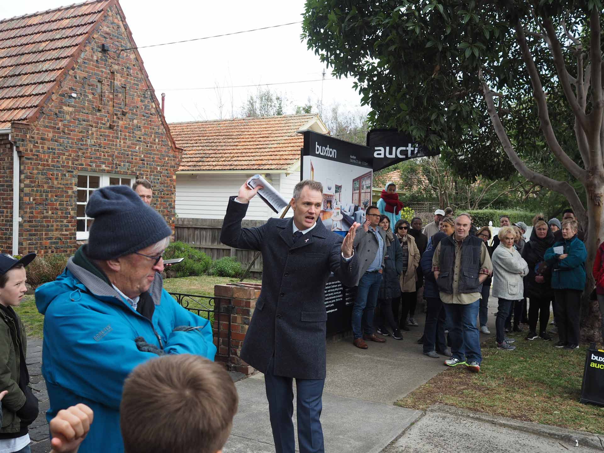 Auction snapshot - Auctioneer calling auction in front of brown brick house